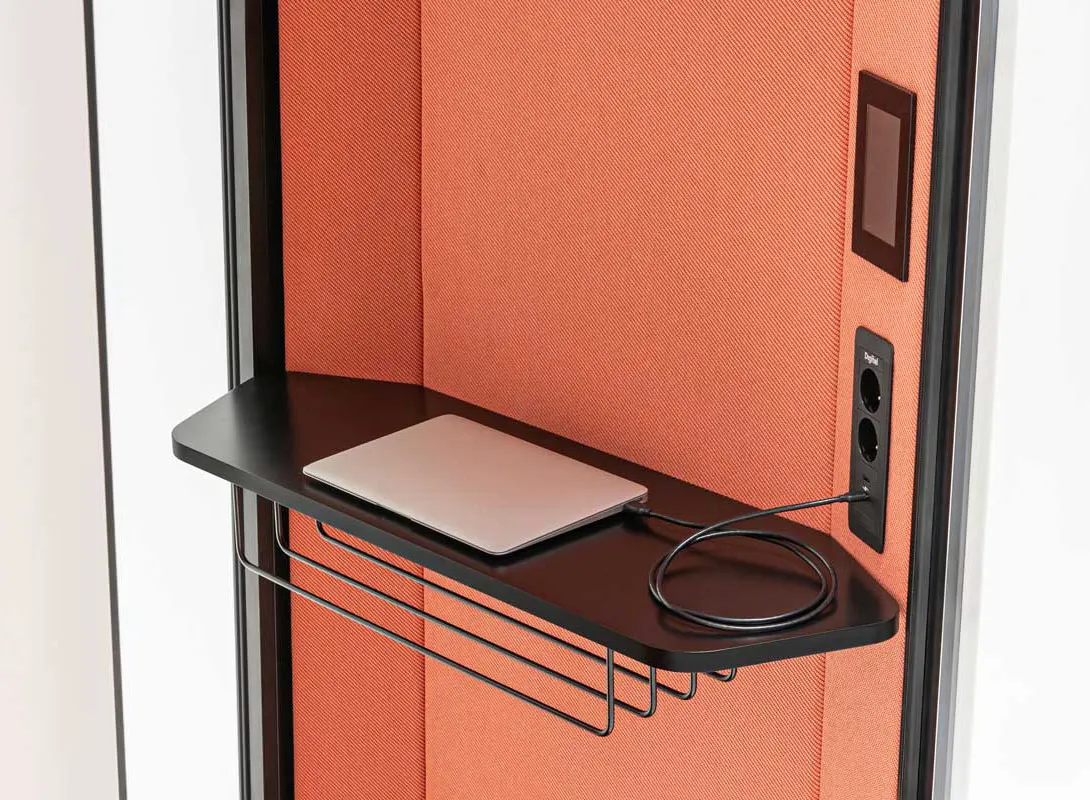 Interior workspace inside Coda booth with charging laptop on the shelf, charging ports and control panel